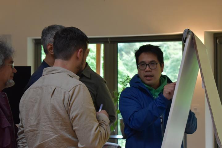 A small group gathered close around a whiteboard, one person pointing at it.