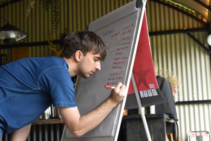 A person leaning in to draw on a flip chart inside a corrugated-iron shed.