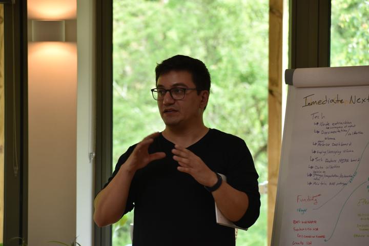 A person presenting in front of a flip chart with their hands pressed together.