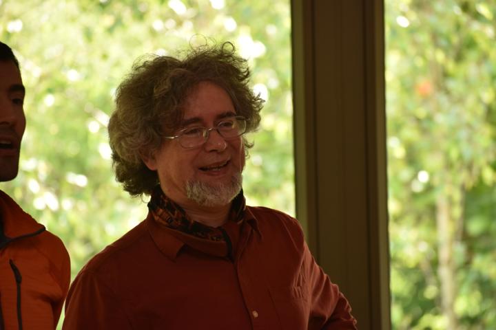 A person in a red shirt smiling, green garden behind them.