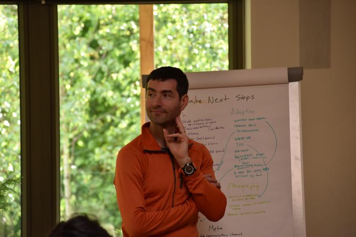 A person in orange standing thoughtfully beside a flip chart of next steps.