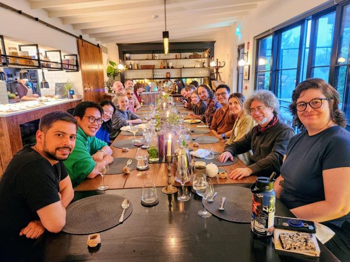 The whole group around one long candlelit dinner table, smiling at the camera.
