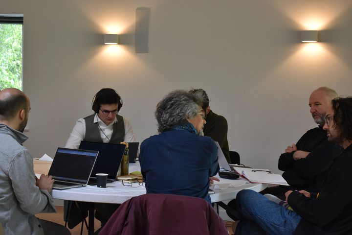 A working group around a table in the round room, laptops open, one person wearing headphones.