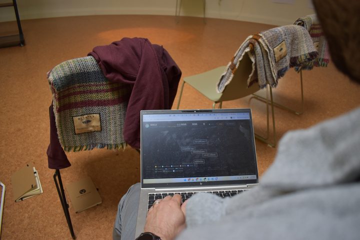 Over the shoulder of a person at a laptop, a graph of linked records on screen, blankets draped over the chairs beyond.