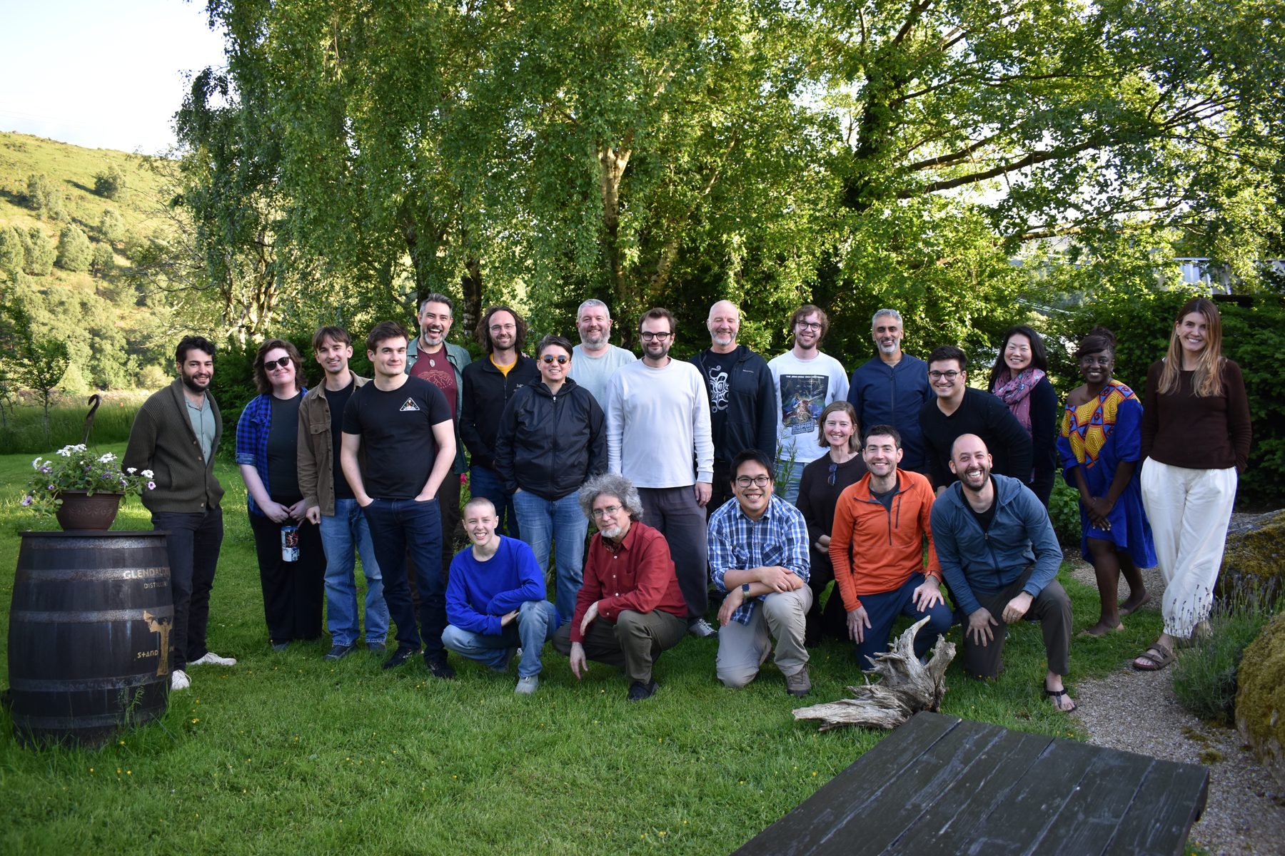 The MIRA Kickoff participants standing and kneeling on a lawn in front of tall trees, smiling at the camera.